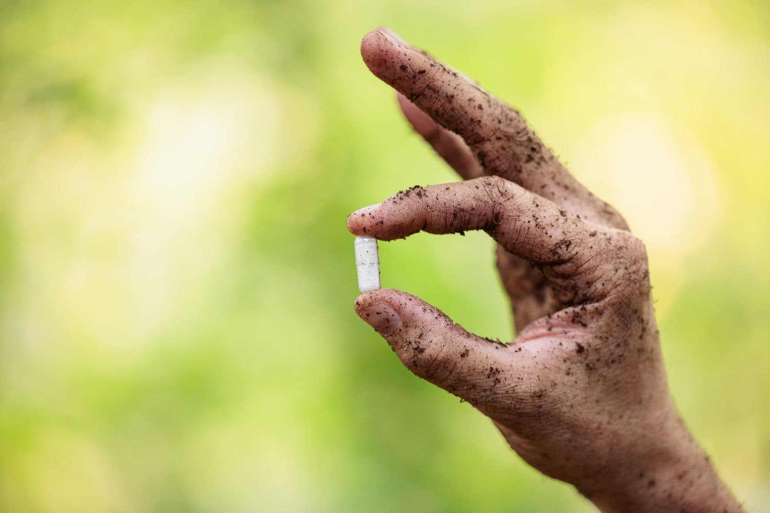 A soil-covered hand holding a microbial capsule