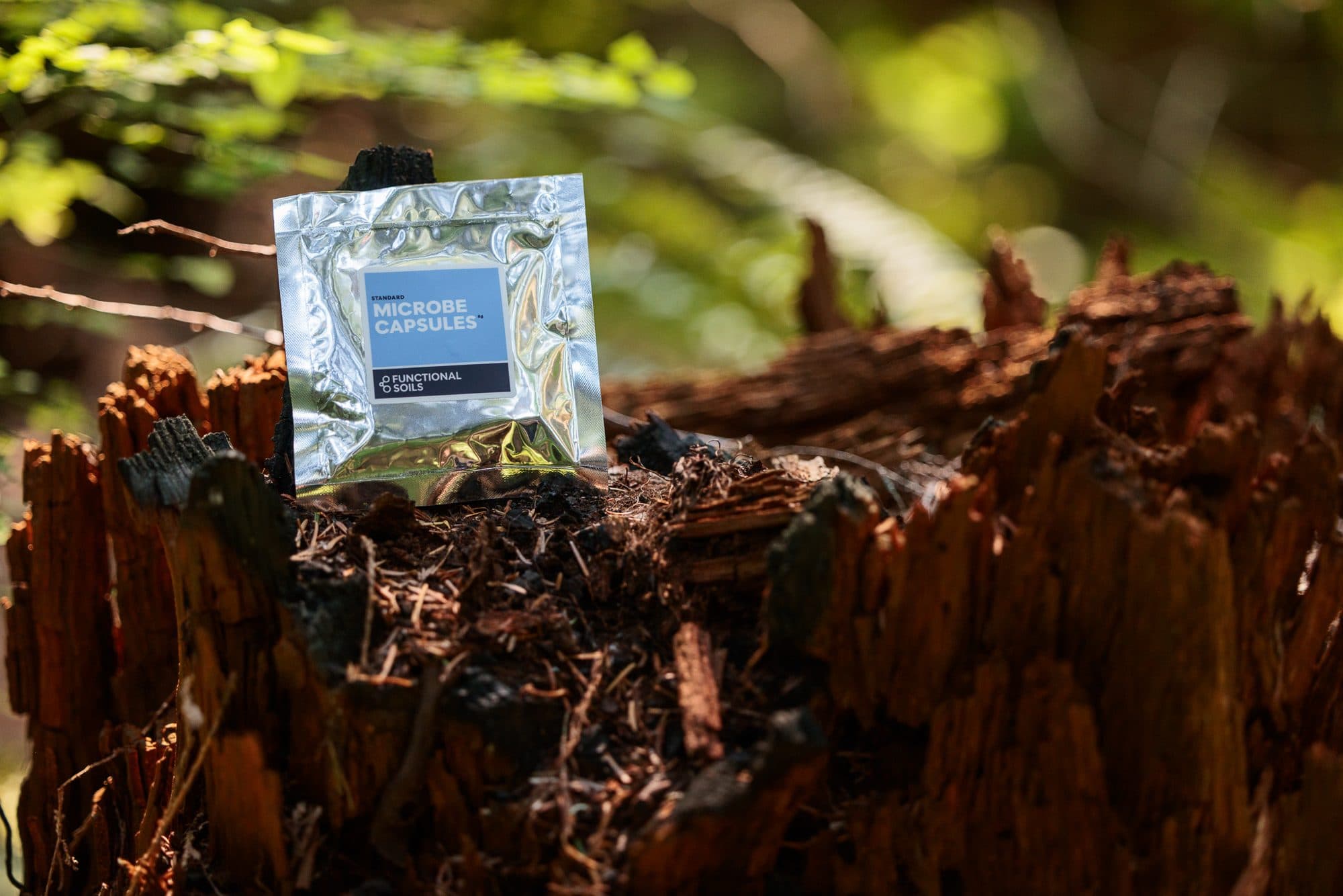 A Microbe Capsules pouch resting on a weathered stump