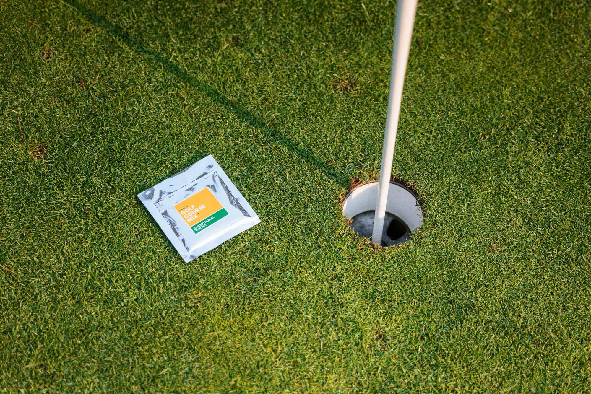 A Golf Course Mix sampler on the green beside the cup and flag
