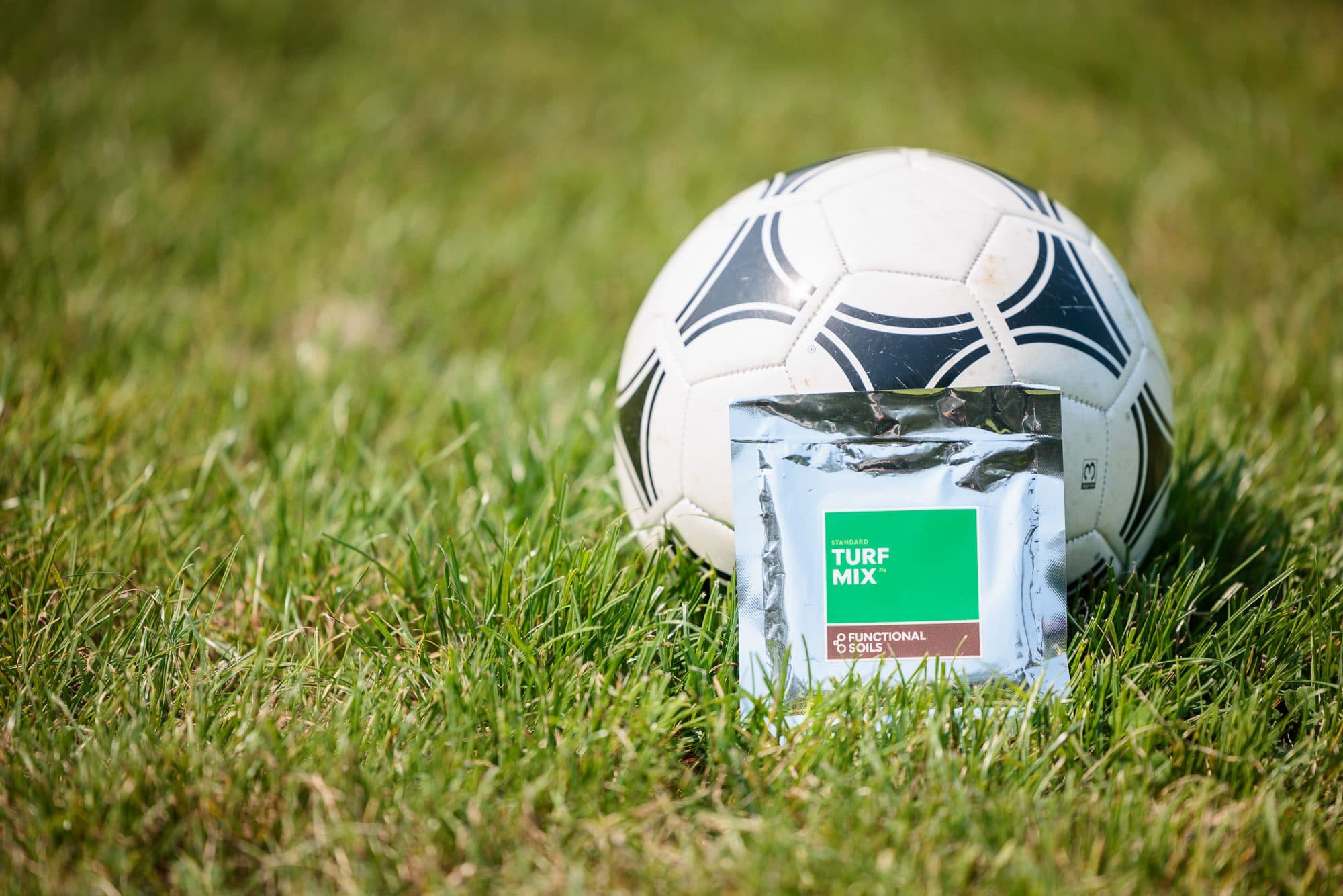 A Turf Mix pouch resting against a soccer ball on the grass