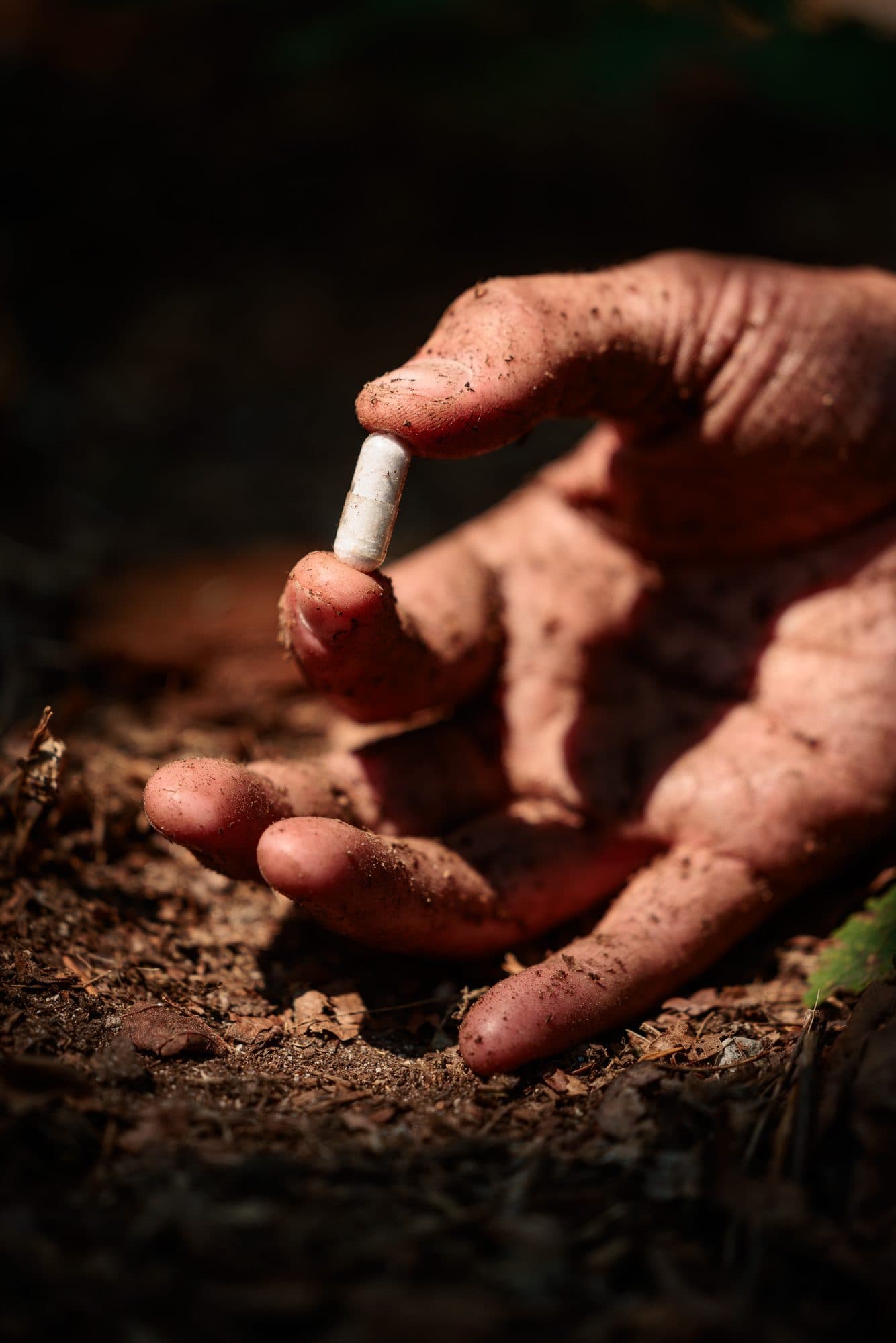 A soil-covered hand placing a microbial capsule into the ground